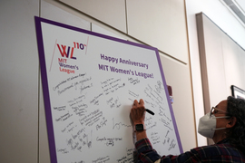 A person writes a message on a poster filled with messages and with a headline that states, “Happy Anniversary MIT Women’s League!”