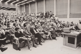 Black-and-white photo of Robert Solow speaking at a lecturn in front of a filled lecture hall