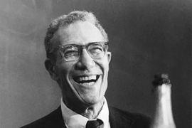 Black-and-white portrait photo of Robert Solow, laughing with a bottle of champagne in front of him