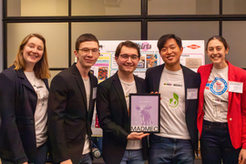 Group photo of five team members wearing blazers, and a person in in middle holds a sign that says, “1st place. Me-Shirts, MADMEC.”