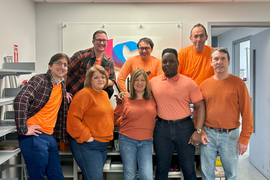Eight Copytech team members wear orange shirts and pose for a photo in their office.