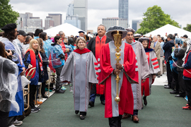 Sally Kornbluth, Noubar Afeyan, Cynthia Barnhart, and other MIT community members wearing academic regalia walk the procession. The person in front is carrying a large golden mace.