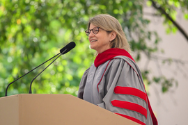 Sally Kornbluth, wearing gray and red academic regalia, speaks at a podium with the MIT seal on the front.