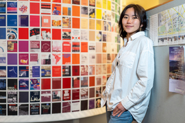 Cindy Xie leans against a partition, and in the blurry background is a grid of posters.