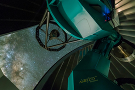 A photo taken from inside the observatory shows the teal telescope pointing up to the stars.