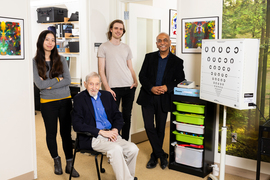 The four researchers pose for a photo in their office next to a boxy machine used to test vision.
