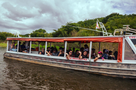 About 30 students wave while on a boat in a river.