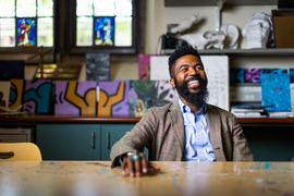 Joshua Bennett at table with colorful paintings behind him