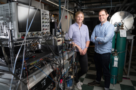 Gabi Wenzel and Brett McGuire stand in the lab full of equipment on racks.