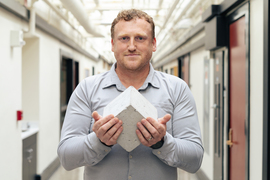 Admir Masic stands in MIT hallway holding a concrete cube. 