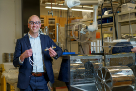 In the lab, Zachary Smith holds the two objects, one like white hair and one like a pipe.