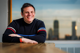 Andrew Babbin sits inside with Boston skyline in background