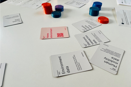 Photo of game chips and cards on a table that say things like “environmental data” and “home improvement.”