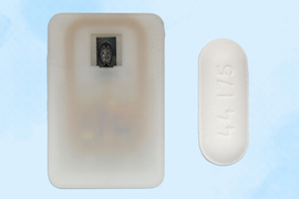 An implantable device next to an oblong pill showing their similar relative size