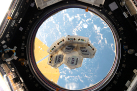 Six hexagonal modular pieces for a side of a ball, floating in space. Through a window is Earth.