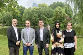 5 people pose together in front of a pond in a verdant park