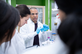 Bryson holds a small pipette while talking to students in lab.