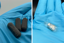Gloved hand holds the pill-shaped capsules. Left is matte black and right is clear with shiny zinc.