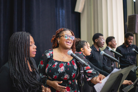 Six MIT Gospel Choir members stand before microphones, singing
