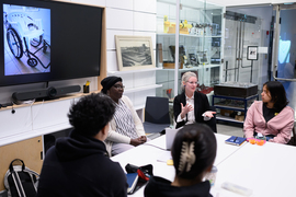 Amy Moran-Thomas sits at a table with students and visitors. 