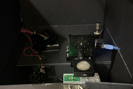 A green light is on a tiny circuit chip, with lens and wires around it.