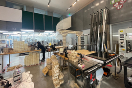 The cluttered fab lab has numerous voxel structures, like an arch, made of different materials.