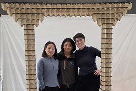 Three people stand under an arch made with voxels.