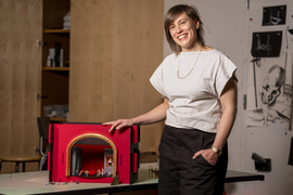 Sara Brown stands next to the stage model, which has a giant golden arch into a red room.
