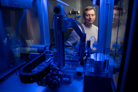 Joey Davis peers through a small blue-lit machine with a robot arm.