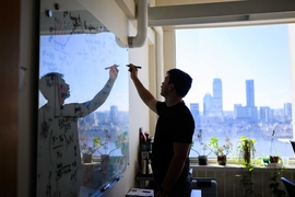 Perrin Davidson, seen in silhouette writing on a whiteboard, with the Charles River and Boston in the background