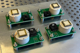 Four flight unit electrospray thrusters, each comprised of a simple circuit board with a small cyllindrical tank, are bolted to a metal sheet
