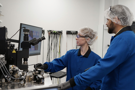 Sarah Spector and Peter Satterthwaite look at a screen while manipulating a microscope