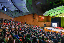 The auditorium is packed as the audience watches a speaker.