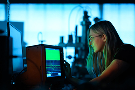 Lanie McKinney looks at glowing green waveforms on an oscilloscope in the lab.