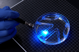 A bright blue light shines on a soft robot in a petri dish.