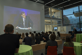 Mark Gorenberg, speaking at the podium, is projected on a wall in the lobby.