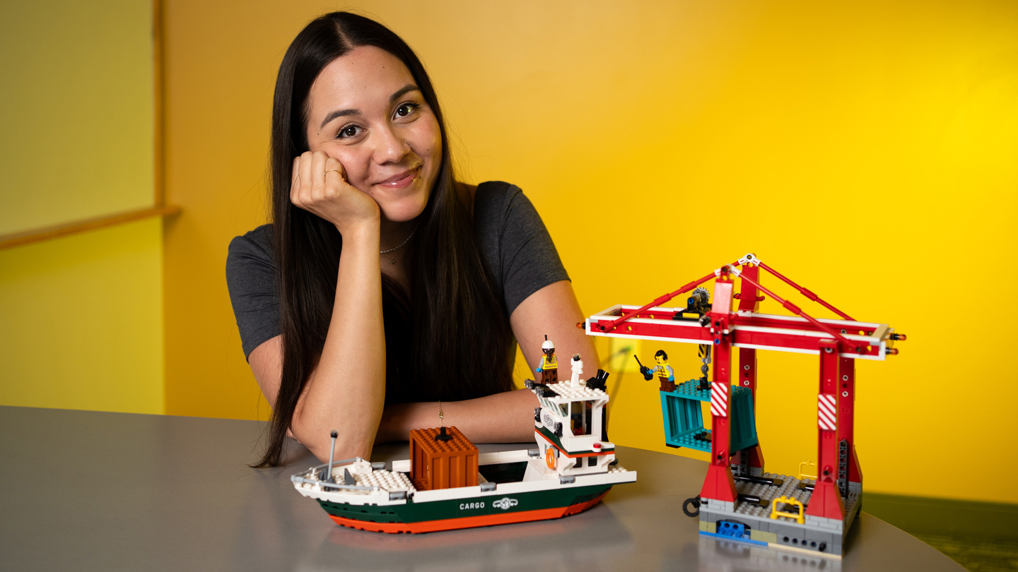 Chelsea Mitchell smiles next to Lego set showing a shipping port with a crane putting containers on a ship.