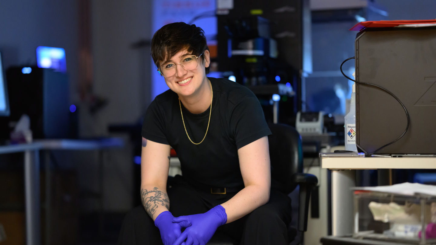 Shannon Knight, wearing nitrile gloves, poses in a chair in her lab