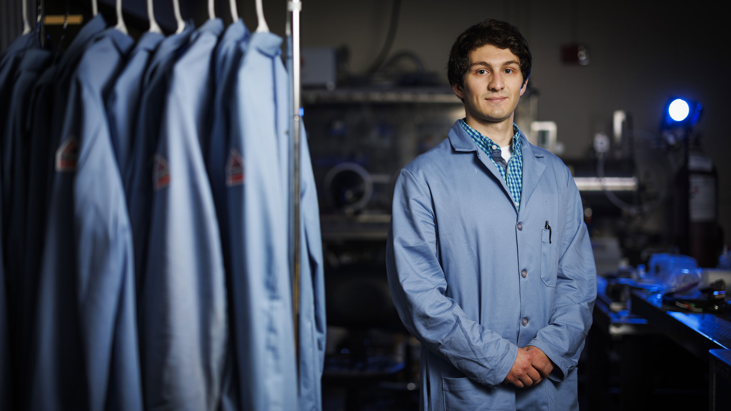 Hugh Smith stands in the lab next to lab coats.
