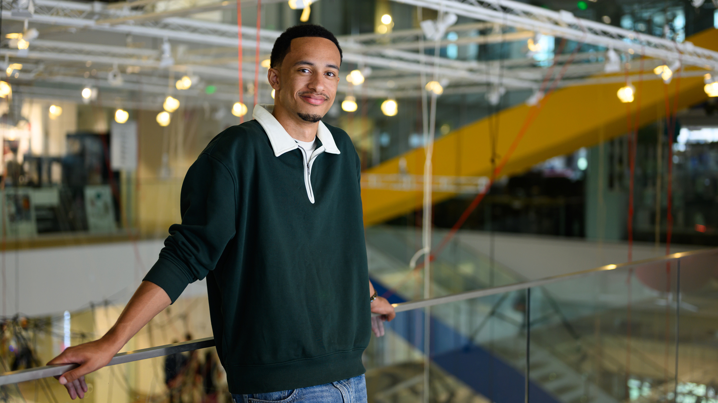 Kayode Dada leans against a glass railing on an atrium walkway