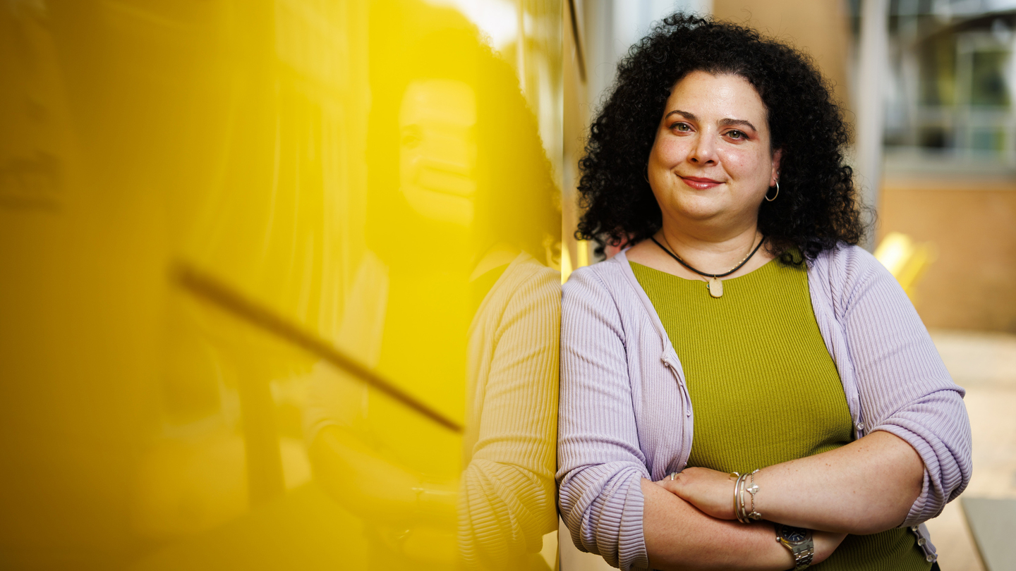 Christina Delimitrou leans against a yellow wall outside of Stata Center.