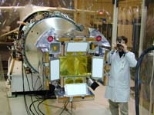 Dr. George R. Ricker, principal investigator for the High-Energy Transient Explorer satellite (HETE-2), takes a photograph during the final inspection of the satellite's soft X-ray cameras. The two dark circles are lens caps covering the optical cameras, and the two curved "ears" behind them are the soft X-ray cameras built at MIT. The four white rectangles on the satellite's front, which is small...