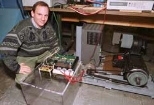 MIT's Dave Perreault kneels next to an alternator that could dramatically increase the power available to future cars. The laboratory-scale apparatus nearest Perreault contains the new switches that enable this increase; the other part of the alternator is at right.