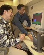 Mechanical engineering graduate student Jung Kim operates the phantom to touch a colleague in London as senior research scientist Mandayam A. Srinivasan watches on-screen representations of each touch.