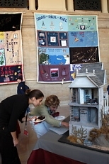 Zoe Malliaros of the Children's AIDS Program at Boston Medical Center (left) and Carolyn Parker, vice chair of the MIT Women's League, check out the sea captain's dollhouse donated by Ronald L. Dion to the Women's League as a raffle item for World AIDS Day to benefit Cambridge Cares About AIDS. Behind them in Lobby 10 are squares from the memorial AIDS quilt.
