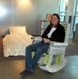 Stephanie Hartman relaxes in a rocking chair she made out of campus phone directories, part of a book-based bedroom suite on view in Rotch Library.
