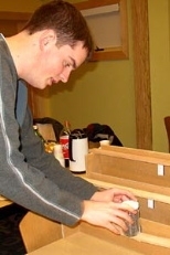 MIT freshman Will Etheridge is loading a beam bending demonstration. The beam on the bottom is made up of 5 thin strips of wood which are not bonded together; the middle beam on the middle shelf has the same 5 strips of wood, but bonded together; and the beam on the top is a single solid piece of wood, of the same dimensions as the other two beams. It has the same deflection as the bonded strips.