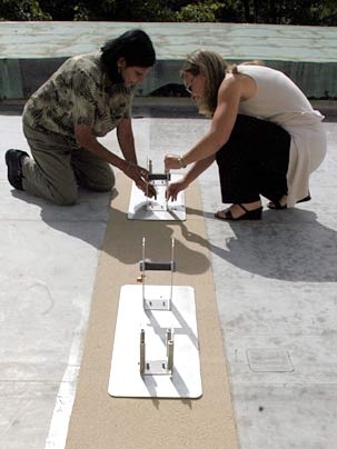 Facilities project manager Laxmi Rao, left, and Heather Denny of the MIT Libraries put down some of the hardware to attach solar panels to the roof of Hayden Library.
