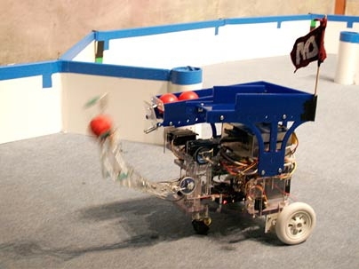 A robot navigates the Maslab course, while attempting to place red balls in 'mouseholes' on the playing field.