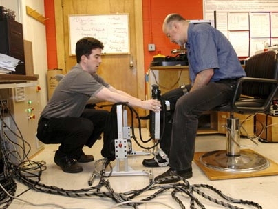 Dustin Williams (MIT S.M. 2001), of Interactive Motion Technologies Inc., helps Hermano Igo Krebs, a principal research scientist in MIT's mechanical engineering department, put on the Anklebot, a robotic device designed to help stroke patients regain movement in paralyzed ankles.